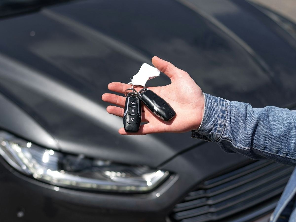 Iemand toont de sleutels van een donkergrijze wagen op een parking