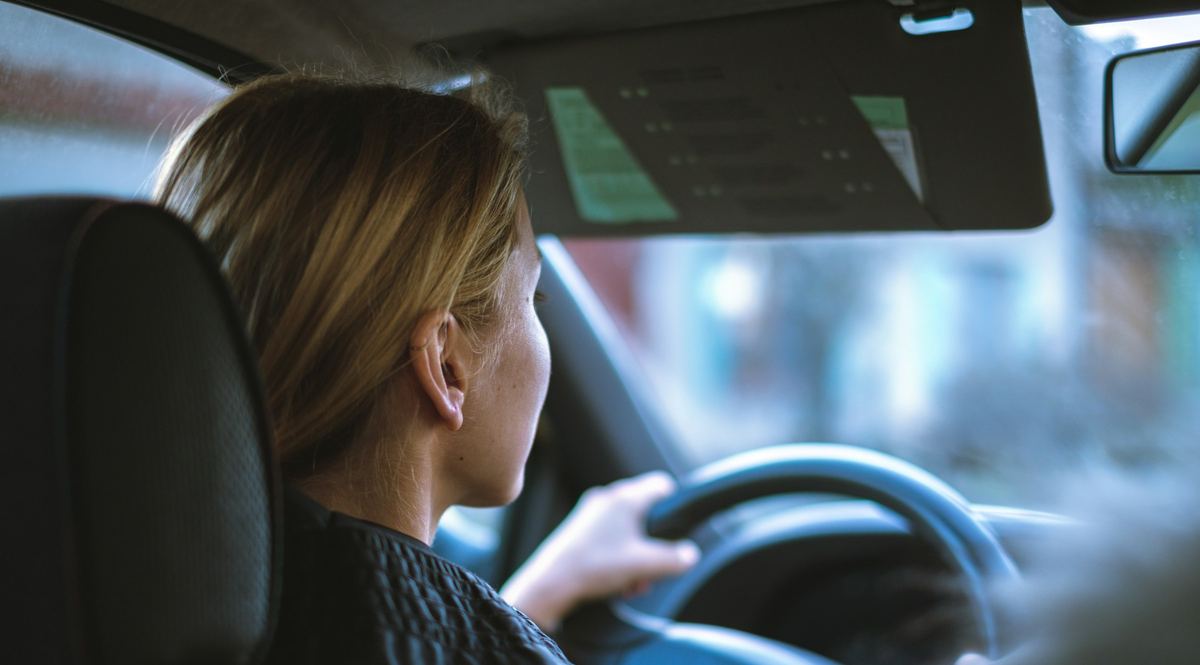 Een vrouw rijdt met een wagen door de stad, gezien van op de achterbank